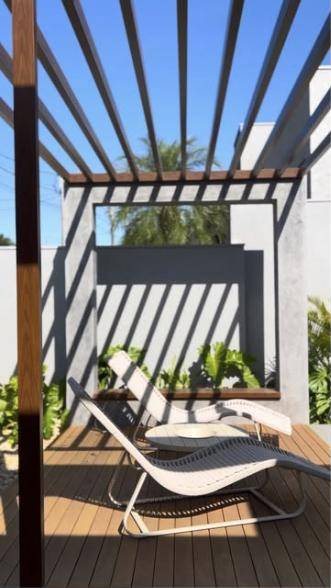 Área externa com pergolado de madeira, espreguiçadeiras e jardim, projeto da AllBe